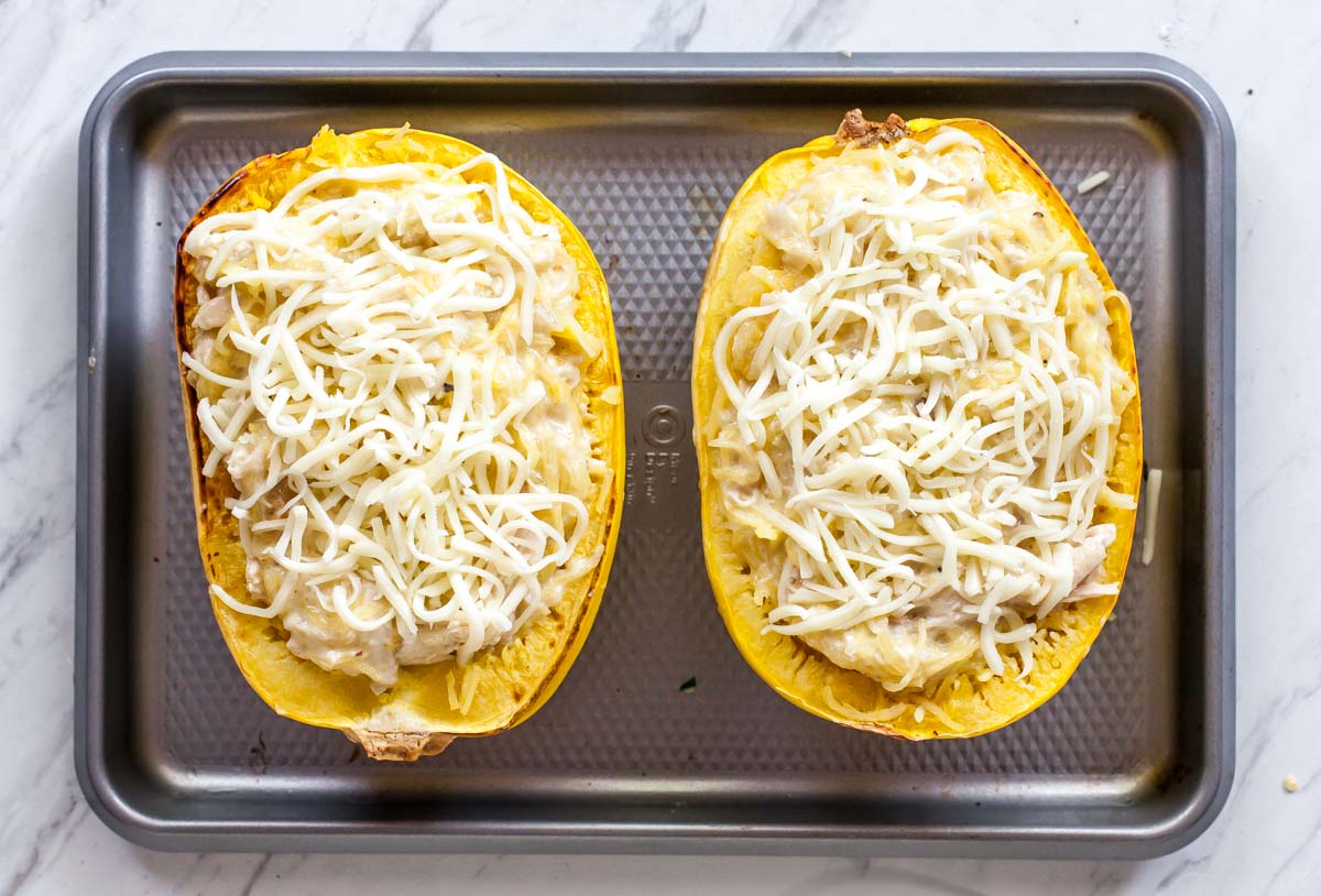 Two spaghetti squash boats on a baking sheet with shredded mozzarella cheese overtop
