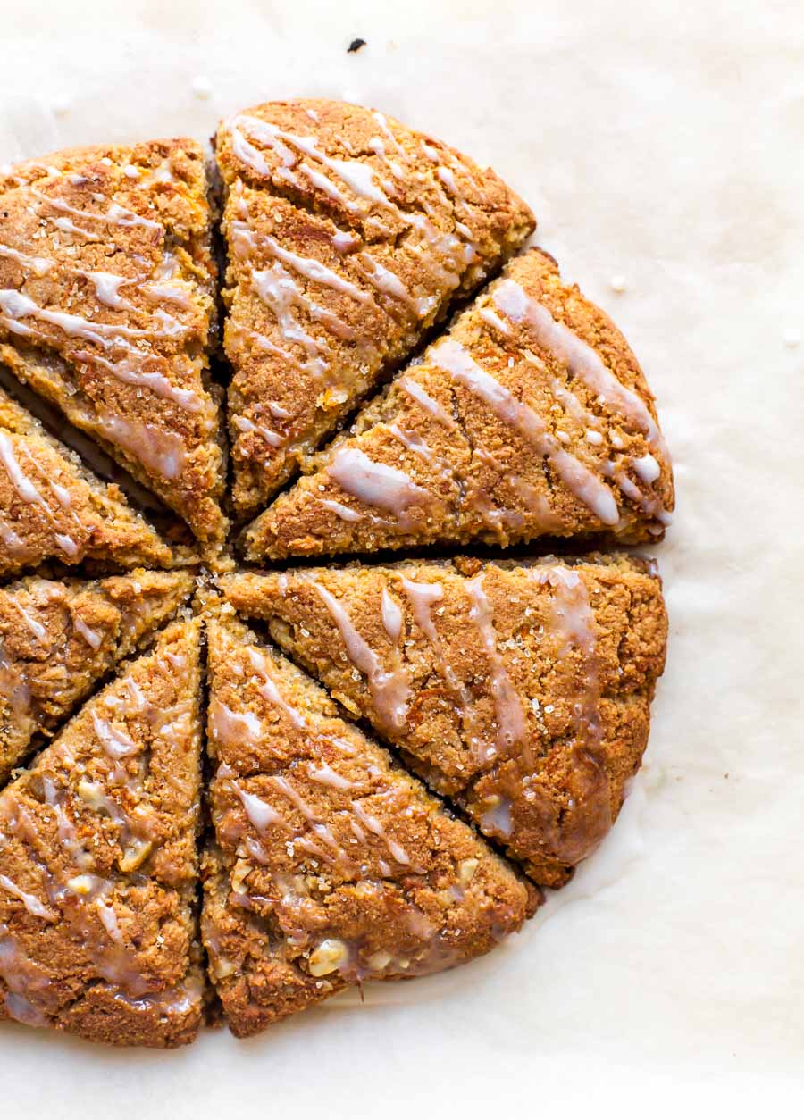 Almond flour scones on a baking sheet being drizzled with orange glaze.