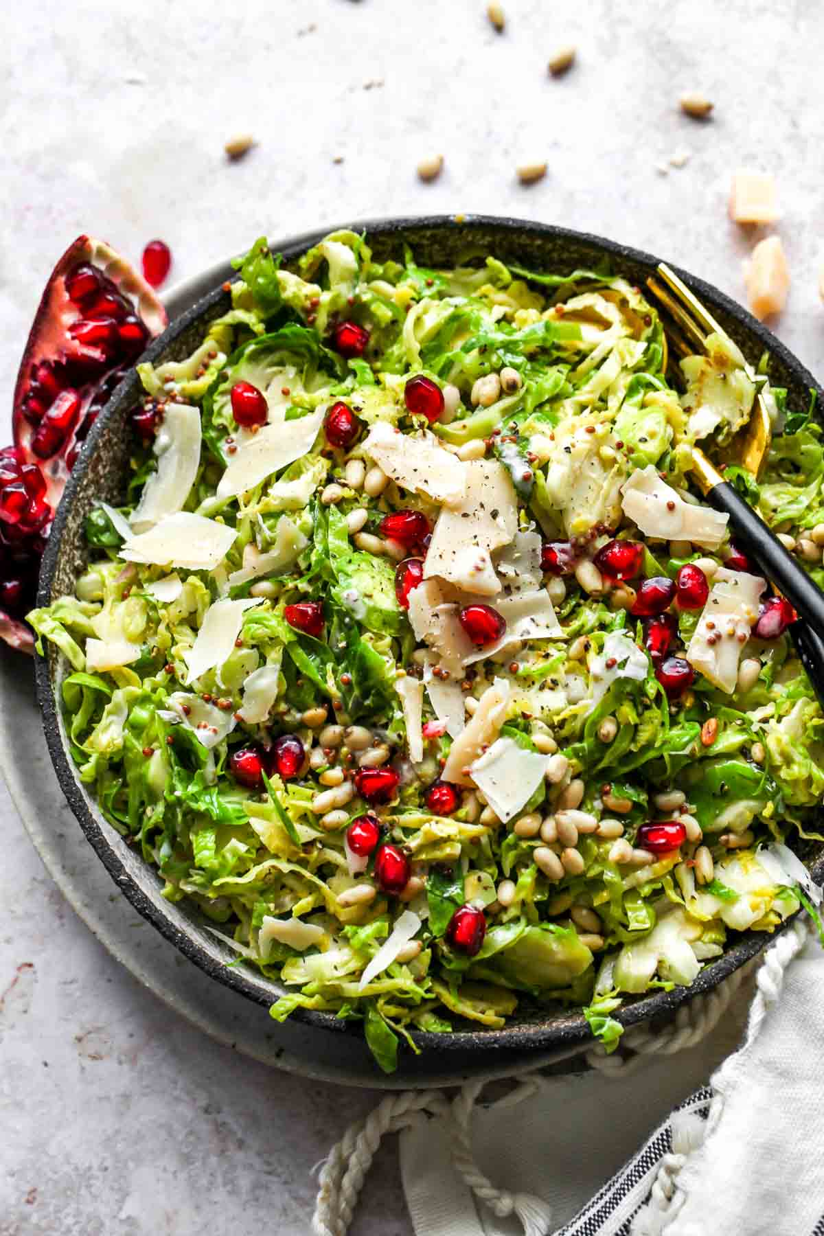 shredded brussels salad topped with pomegranate and parmesan in a serving bowl