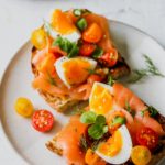 Smoked Salmon Niçoise Toast sliced in half arranged on a white plate.