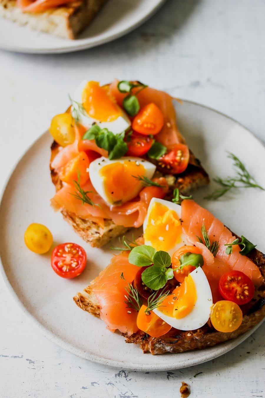 Smoked Salmon Niçoise Toast sliced in half arranged on a white plate.