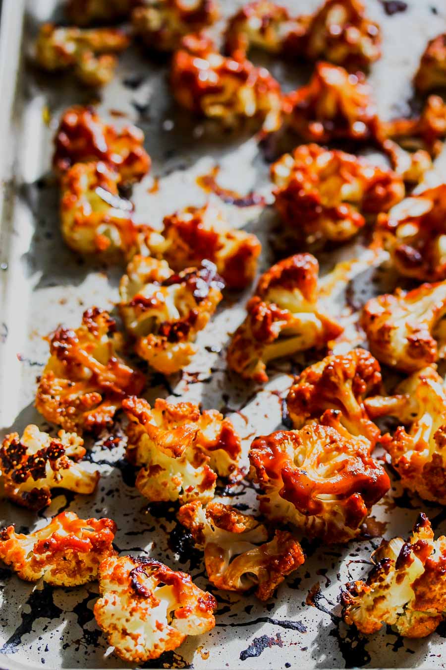 Cauliflower florets being topped with BBQ sauce on a sheet pan