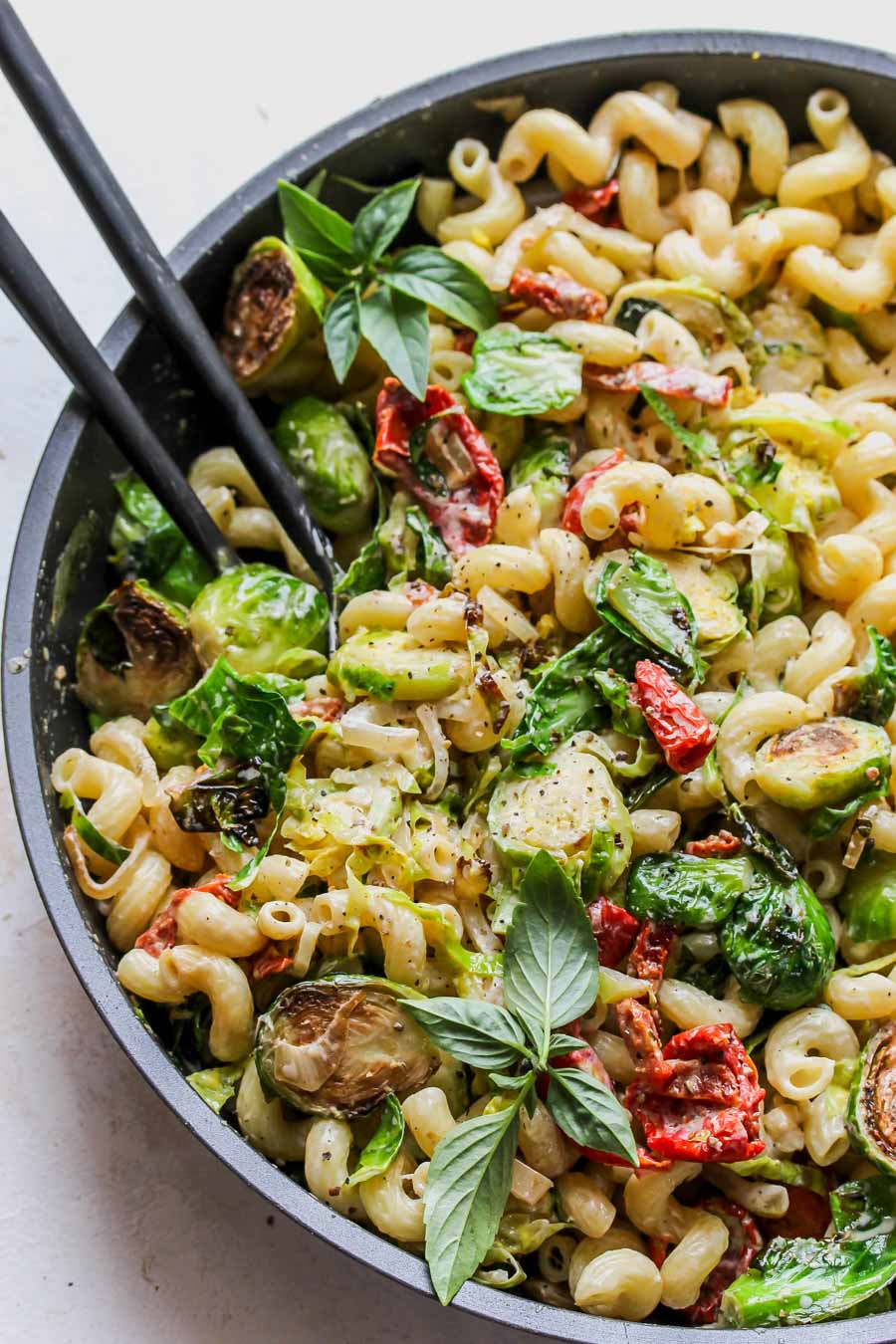 Pasta being tossed with veggies and sauce in a skillet