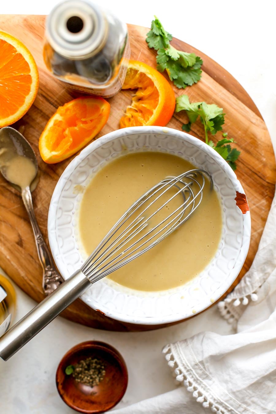Orange-sesame miso dressing being mixed in a small white bowl on a cutting board.
