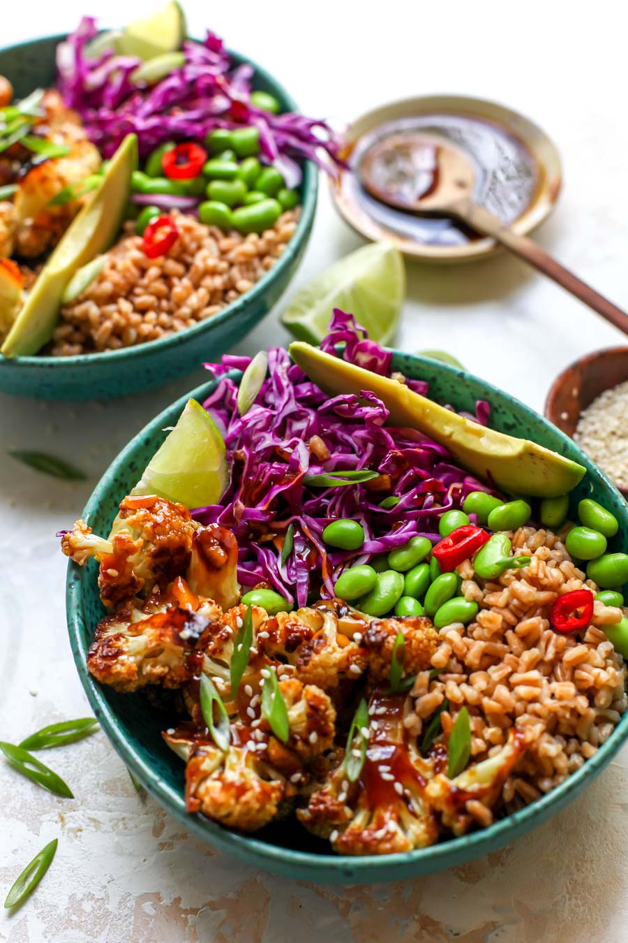 Teriyaki cauliflower bowls styled in two teal bowls with avocado wedges and green onion on top.