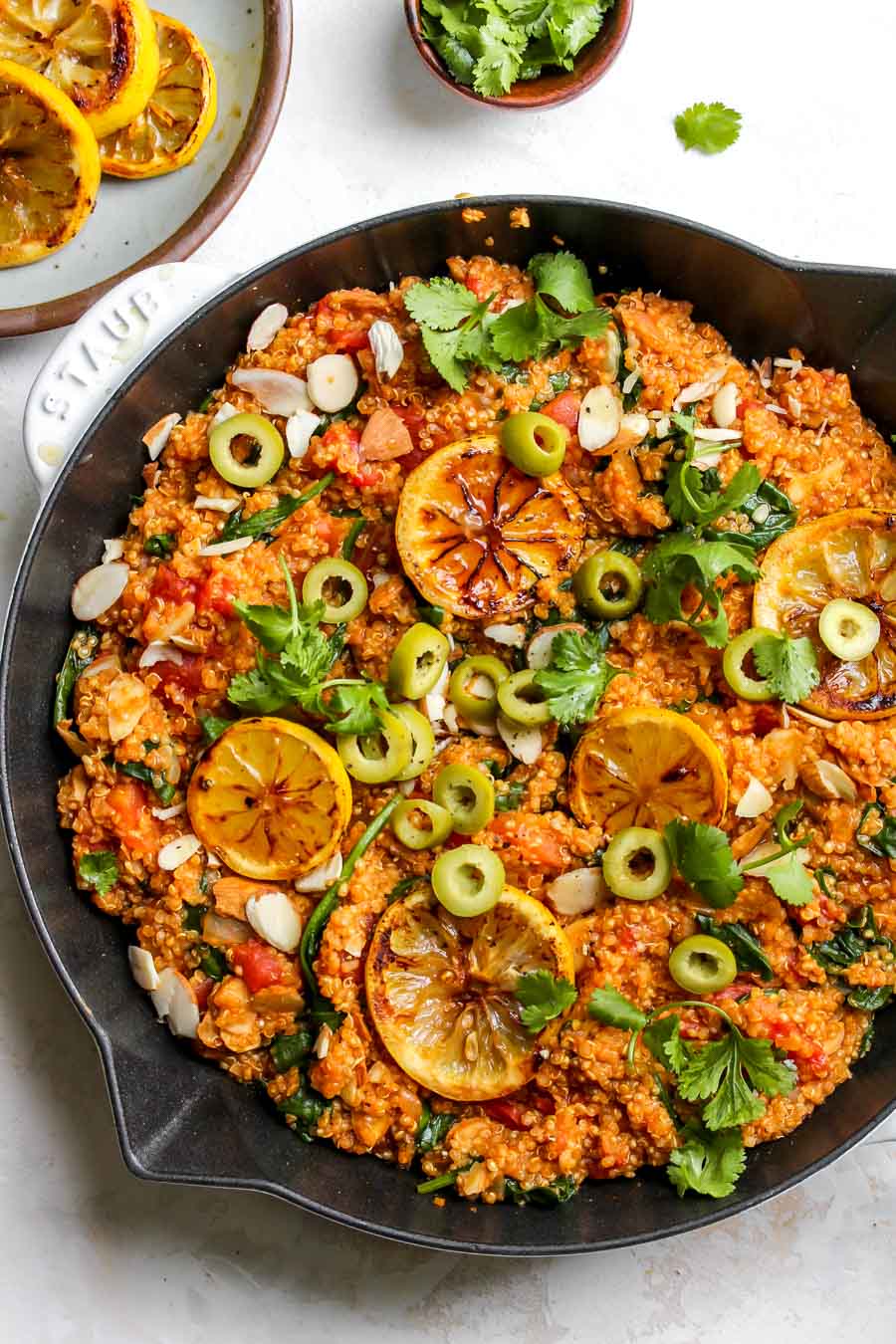 Moroccan Quinoa in a white skillet topped with lemon slices and harbs.