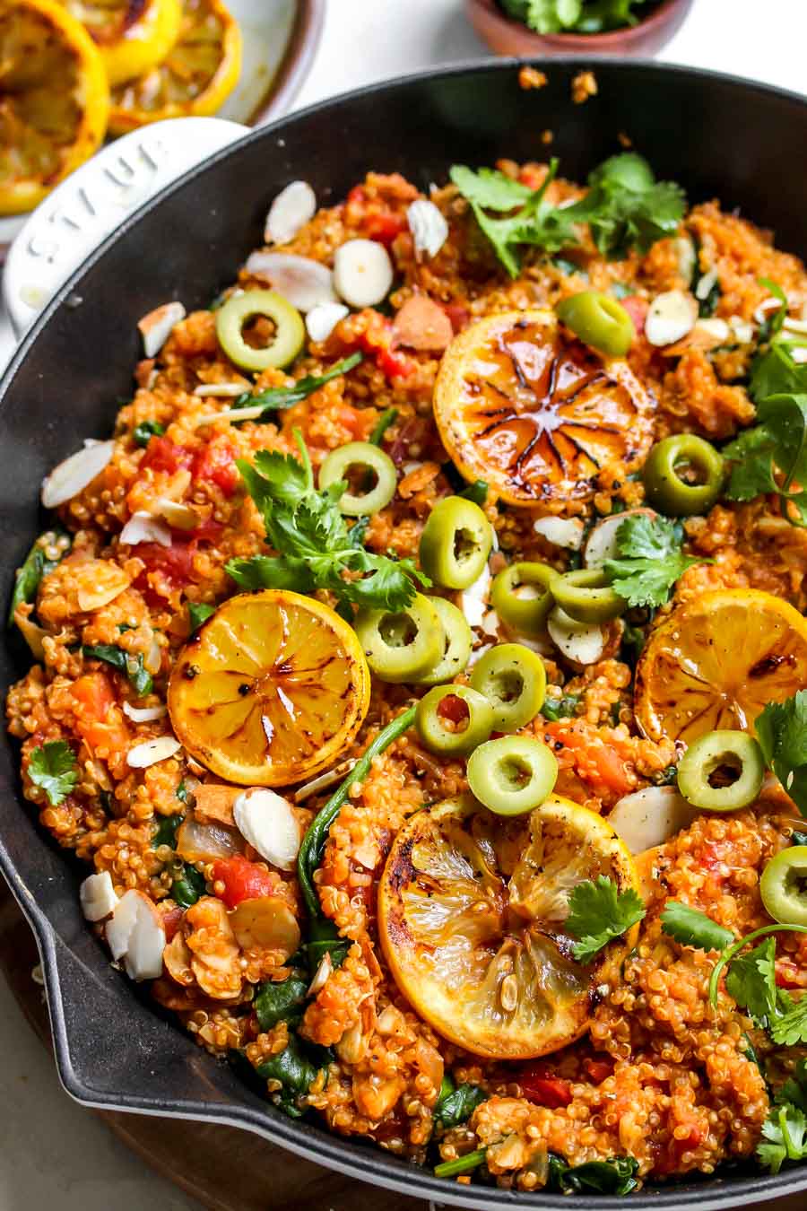 Quinoa dish being garnished with lemon slices, olives, parsley, and almonds.