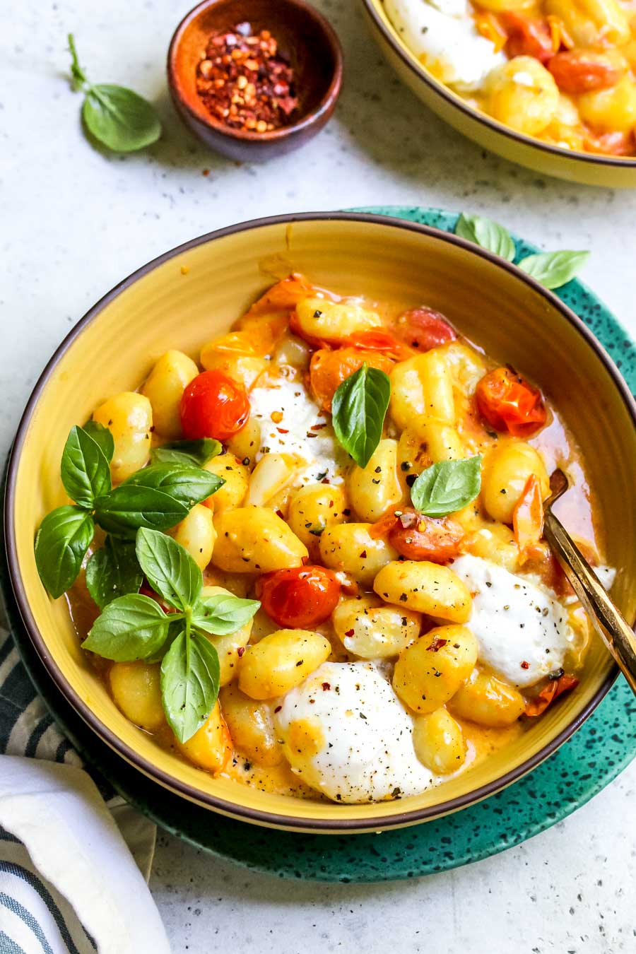 A yellow bowl filled with creamy tomato gnocchi and topped with fresh basil leaves.