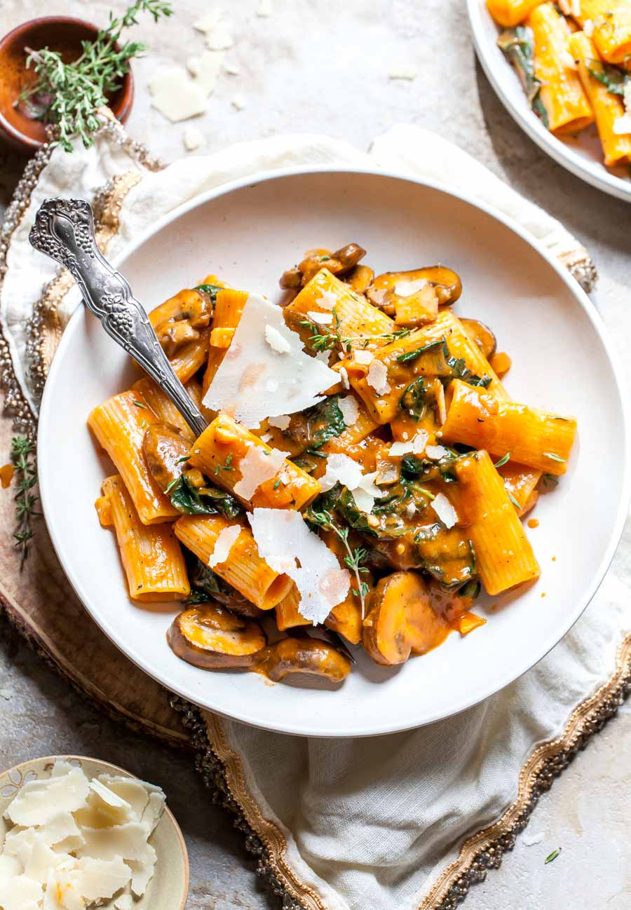 Pumpkin pasta styled in a white bowl topped with shredded Parmesan cheese and thyme.