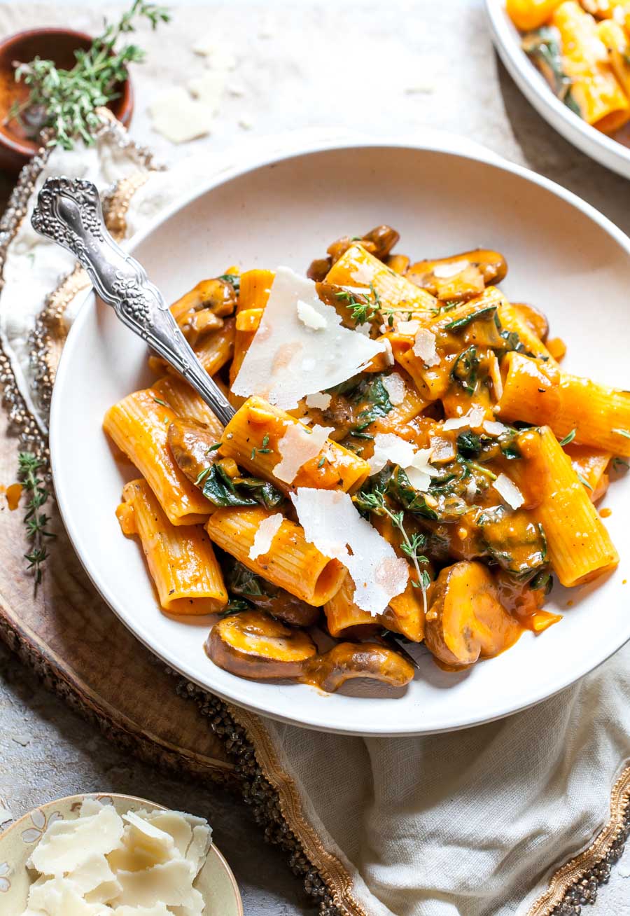 Pumpkin pasta in a white pasta bowl garnished with Parmesan and fresh thyme.
