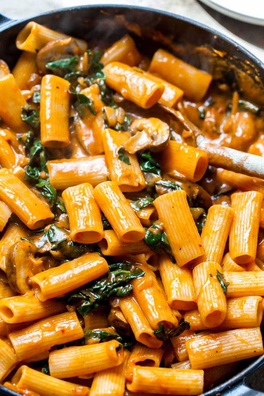 Rigatoni being tossed in vodka sauce in a large pot.