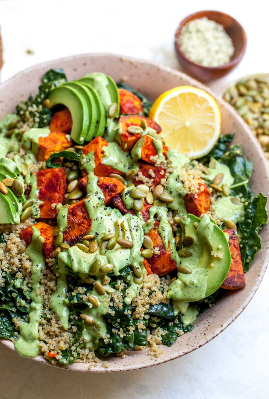 Sweet potato quinoa salad in a pink serving bowl topped with avocado slices and lemon