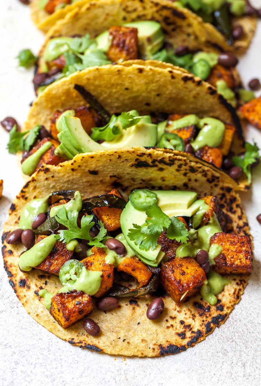 Three tacos lined up against each other on a white surface.