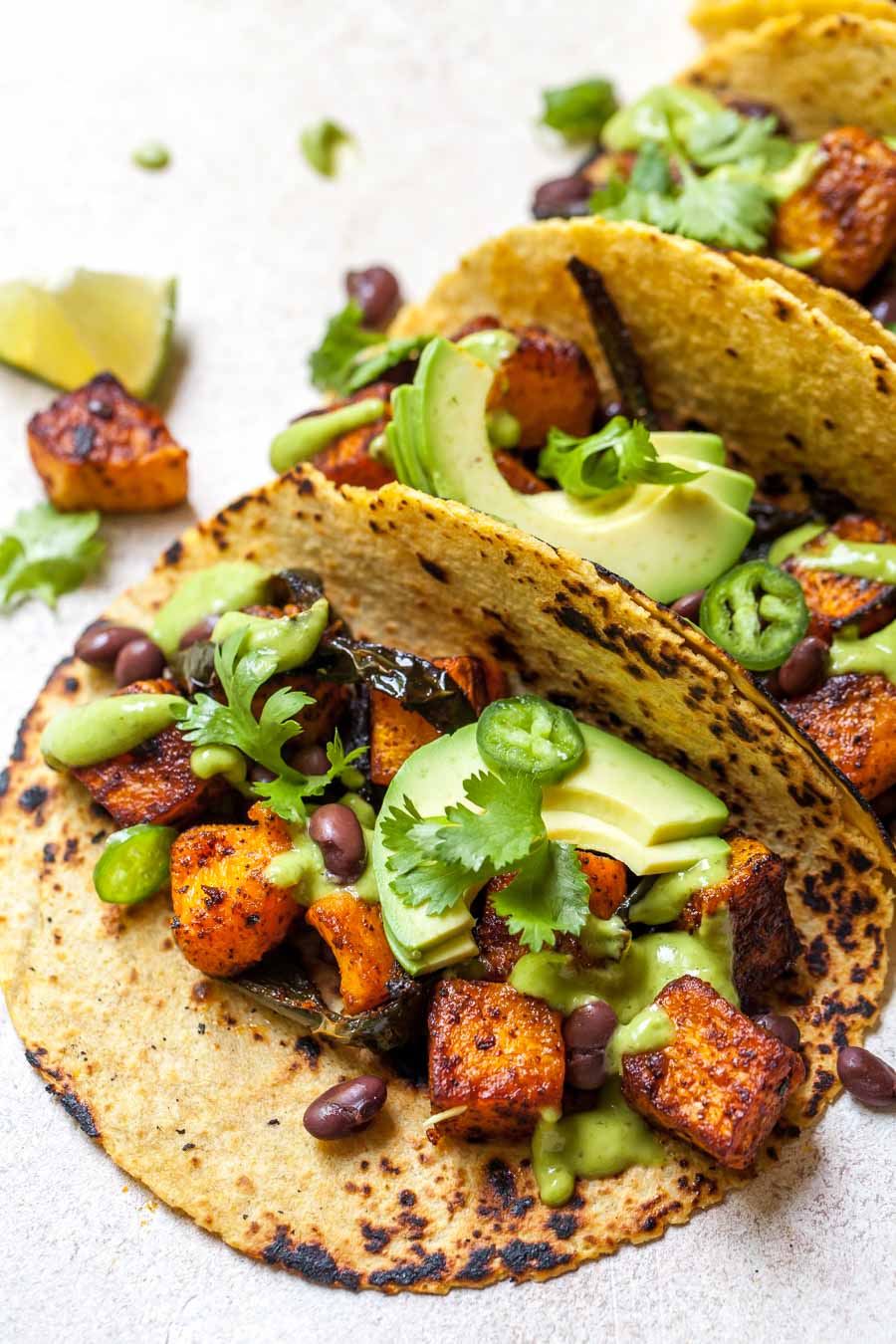 Butternut squash tacos assembled and topped with avocado sauce on a white surface.