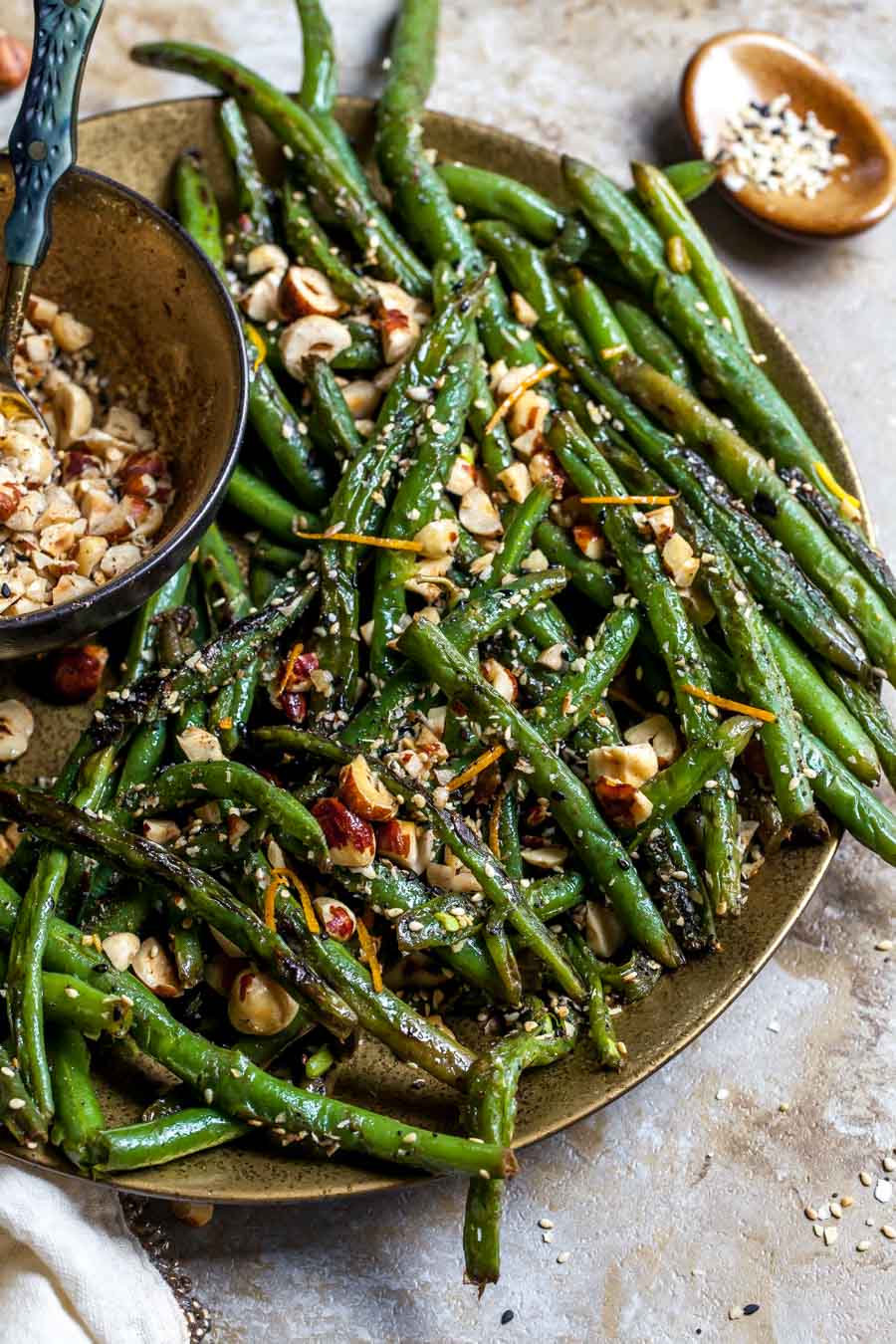 Green beans cooked in browned butter and topped with toasted hazelnuts arranged on a gold plate.
