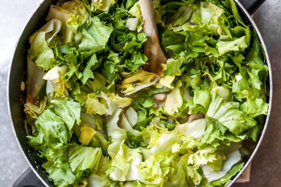 Chopped escarole being stirred into soup mixture