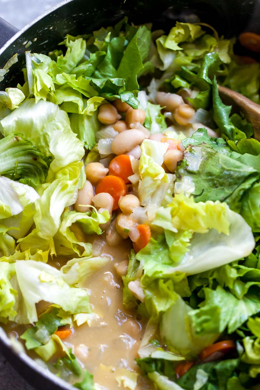 Escarole, beans, and broth being stirred into white bean escarole soup