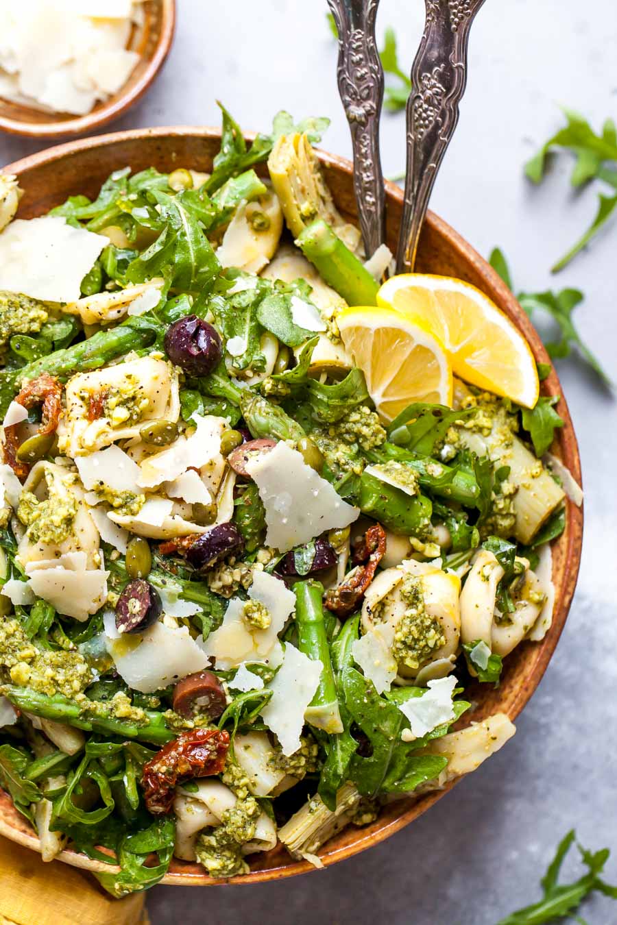 Pesto tortellini pasta salad arranged in a serving bowl topped with lemon wedges