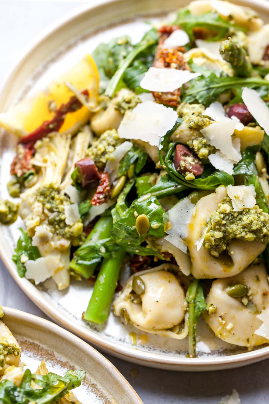 Pesto tortellini pasta salad arranged on a serving plate topped with parmesan
