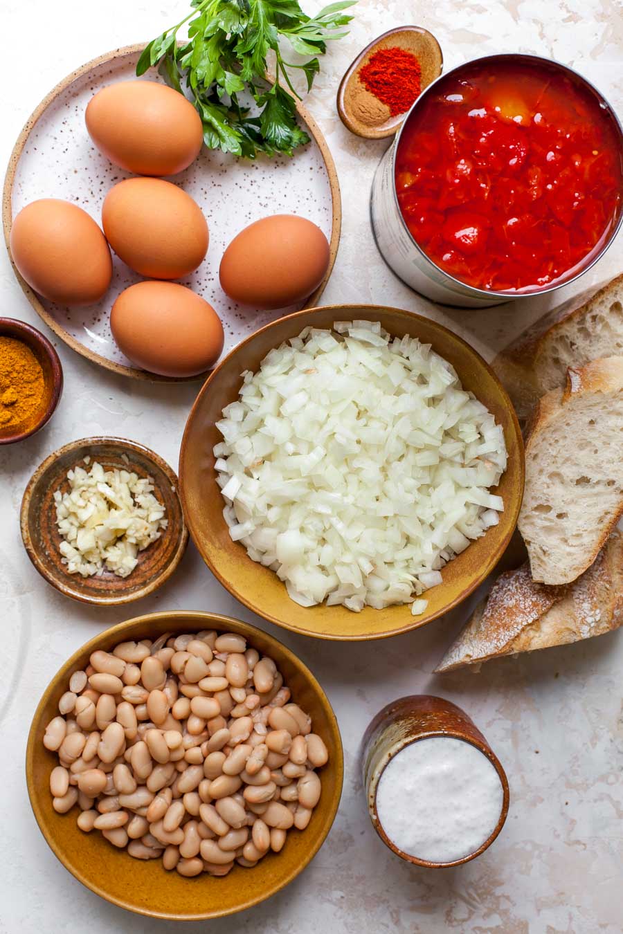 Ingredient overhead shot featuring eggs, spices, onions, tomatoes, and bread