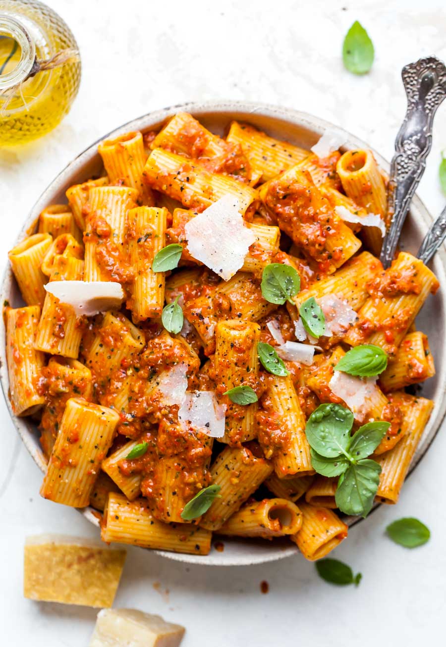 Red pesto pasta in a white serving bowl topped with basil and Parmesan.
