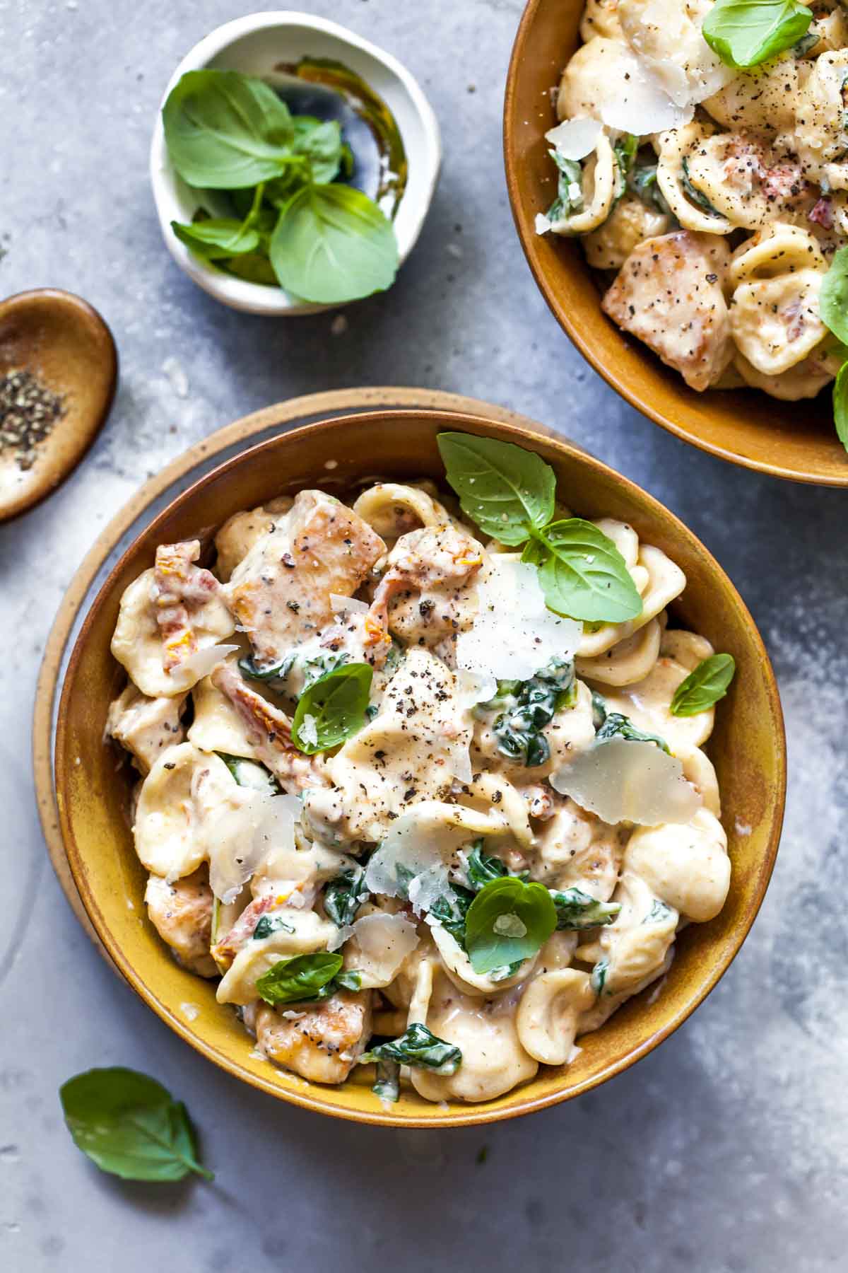 Chicken florentine pasta in a gold bowl topped with basil leaves and Parmesan shavings