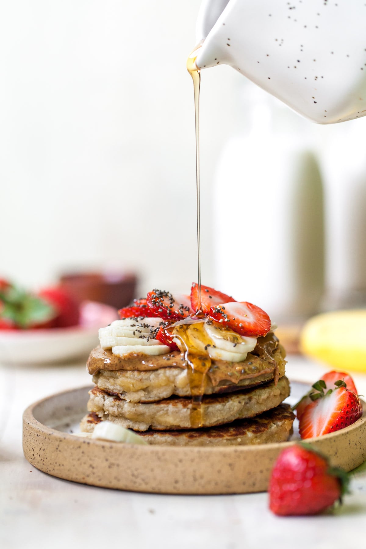 Syrup actively pouring over a stack of three pancakes on a plate