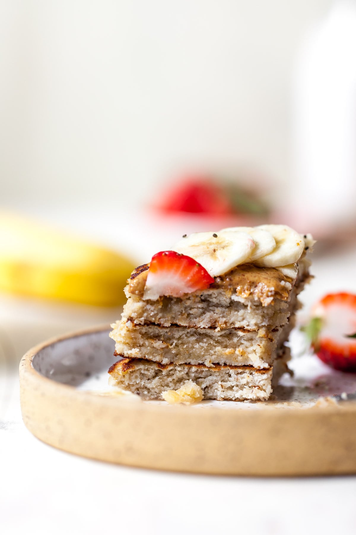 One bite of coconut flour pancakes on a plate topping with banana and strawberry slices