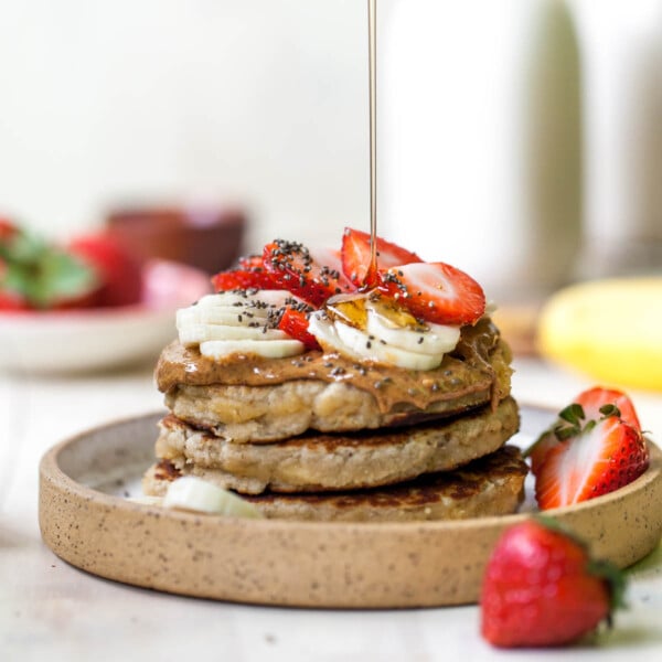 Stack of three coconut flour pancakes on a plate with syrup drizzle overtop