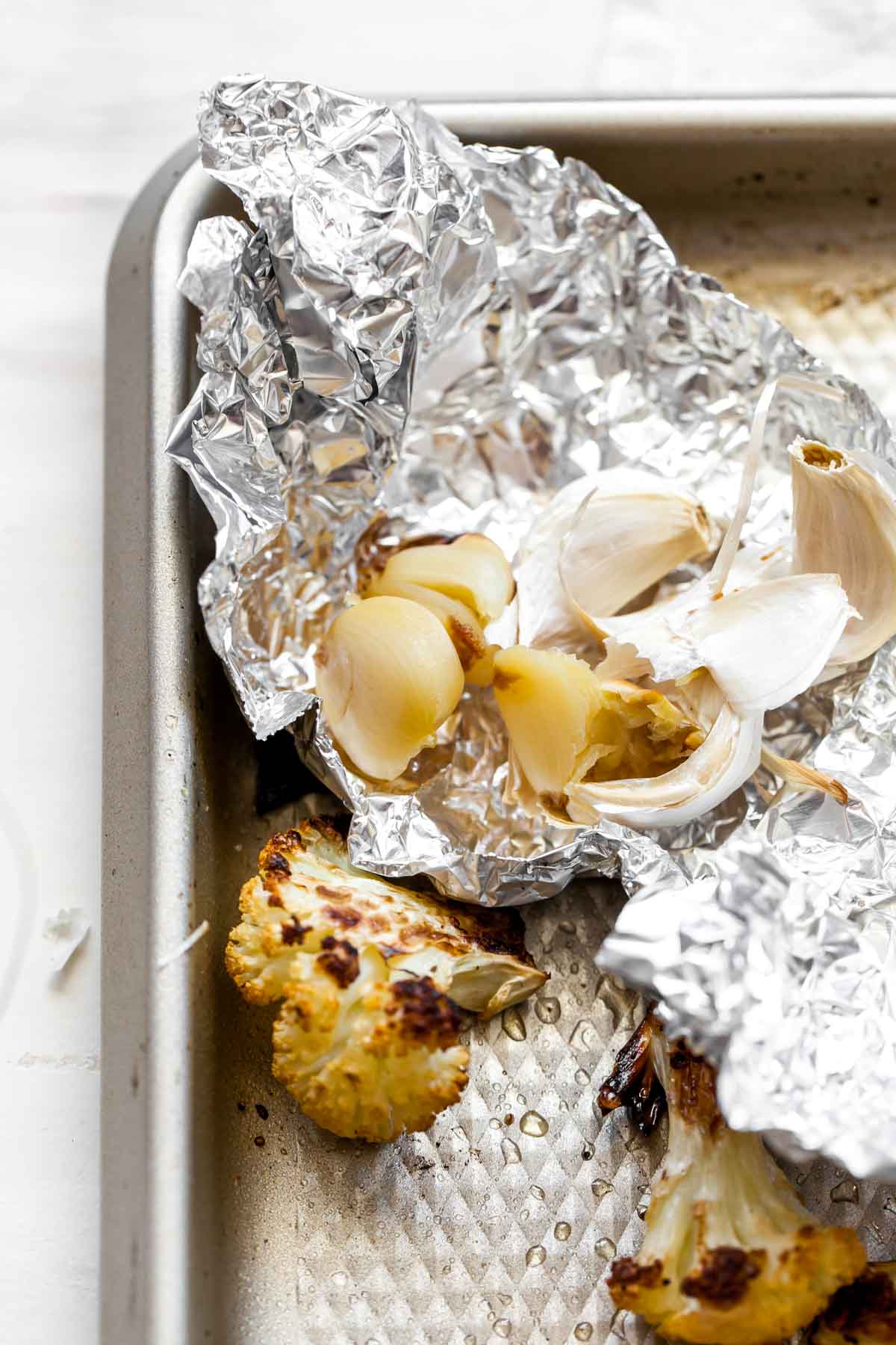 Garlic cloves in tin foil in the corner of a baking sheet