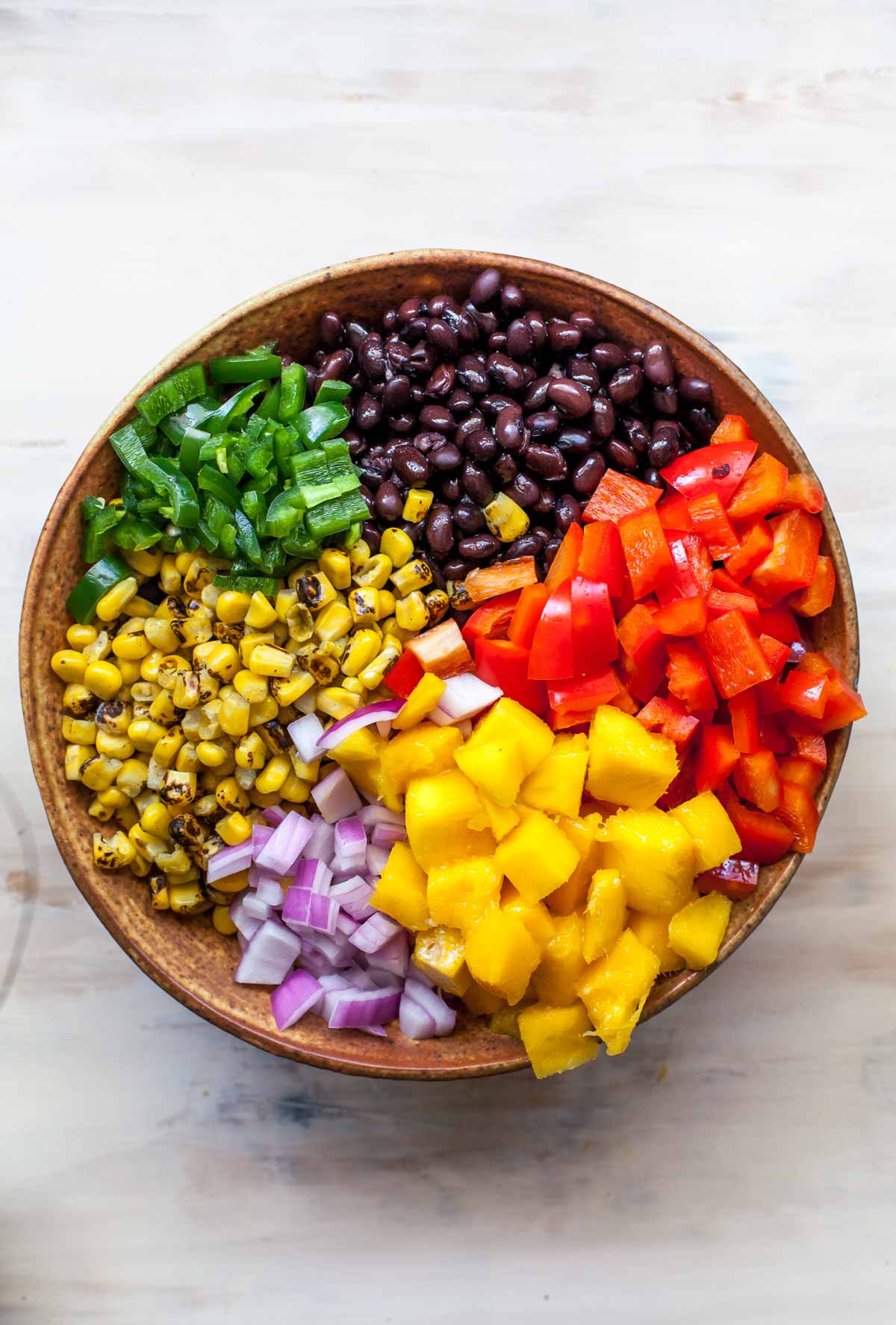 Quinoa, mango, black beans, corn, and bell peppers in a large brown bowl