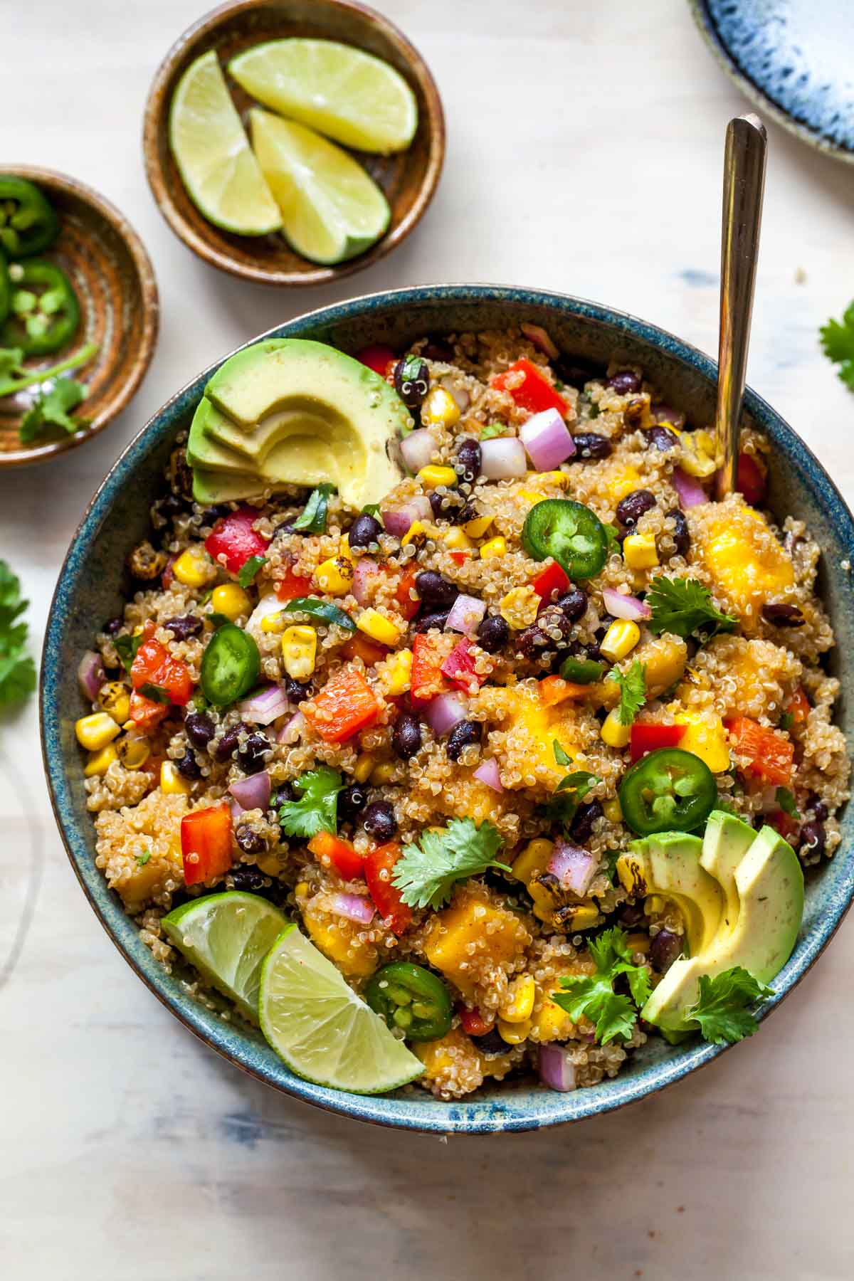 Quinoa, mango, and veggies in a bowl topped with lime wedges and avocado slices