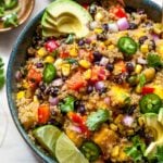 Quinoa, mango, and black bean salad in a black bowl topped with sliced avocado