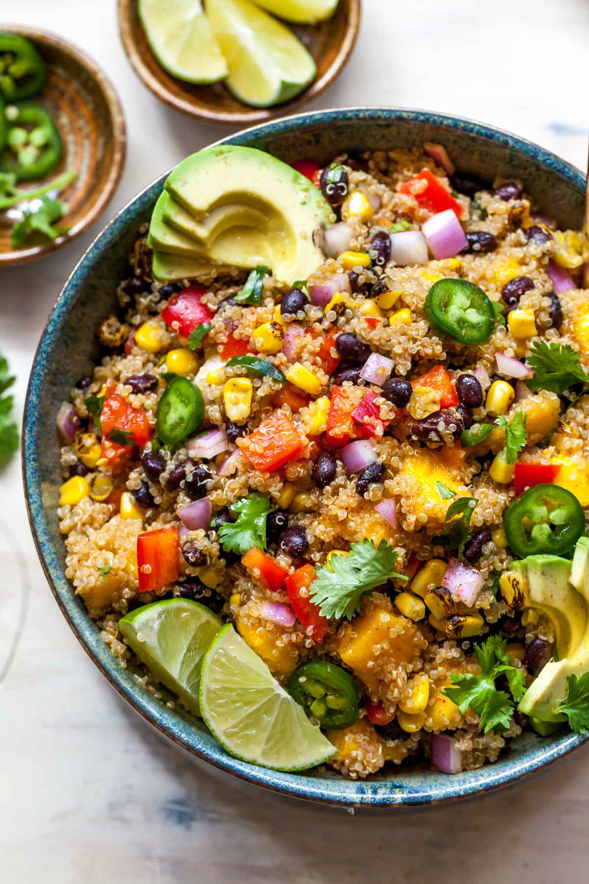 Quinoa, mango, and black bean salad in a black bowl topped with sliced avocado