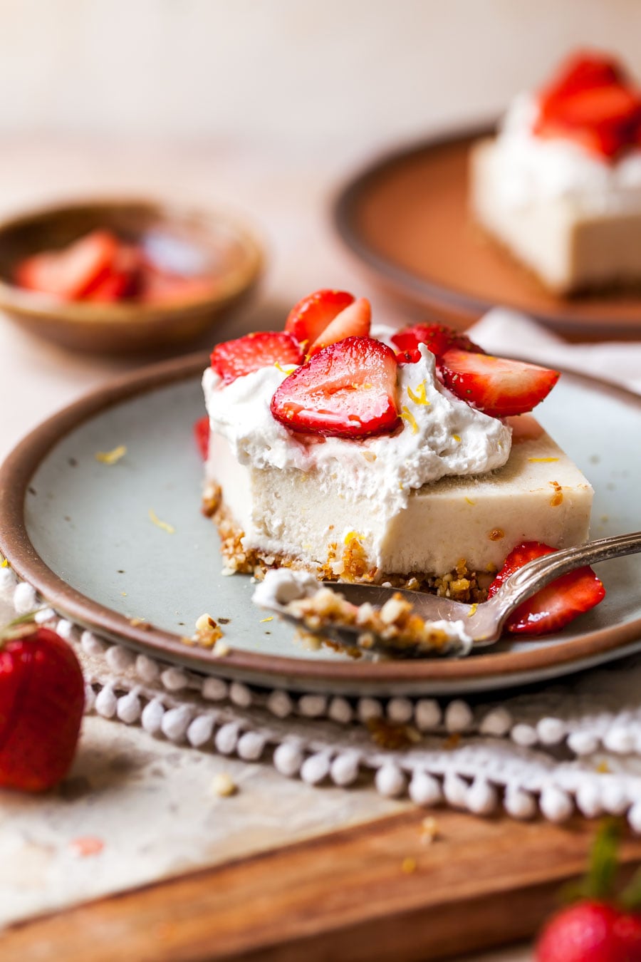 Vegan strawberry cheesecake bar on a blue plate with a spoon resting on the plate.