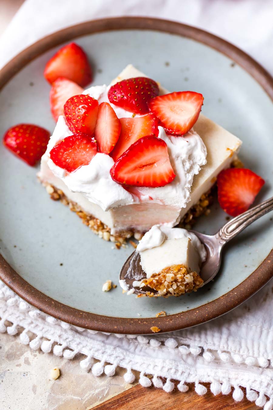 Sliced strawberries and whipped topping being added to a cheesecake bar.
