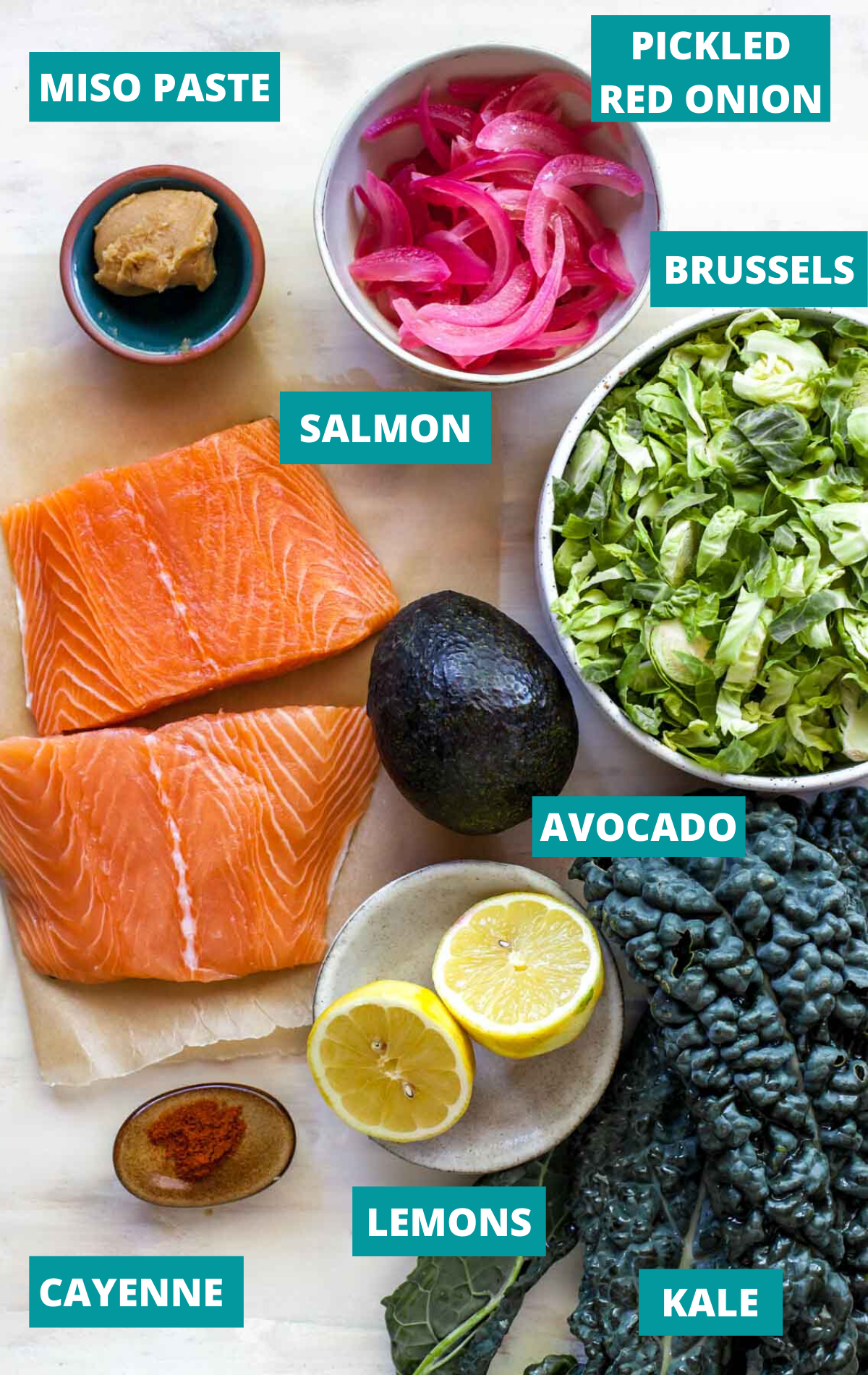 Salmon fillets, kale, brussels, and salad dressing ingredients in separate bowls with ingredient labels