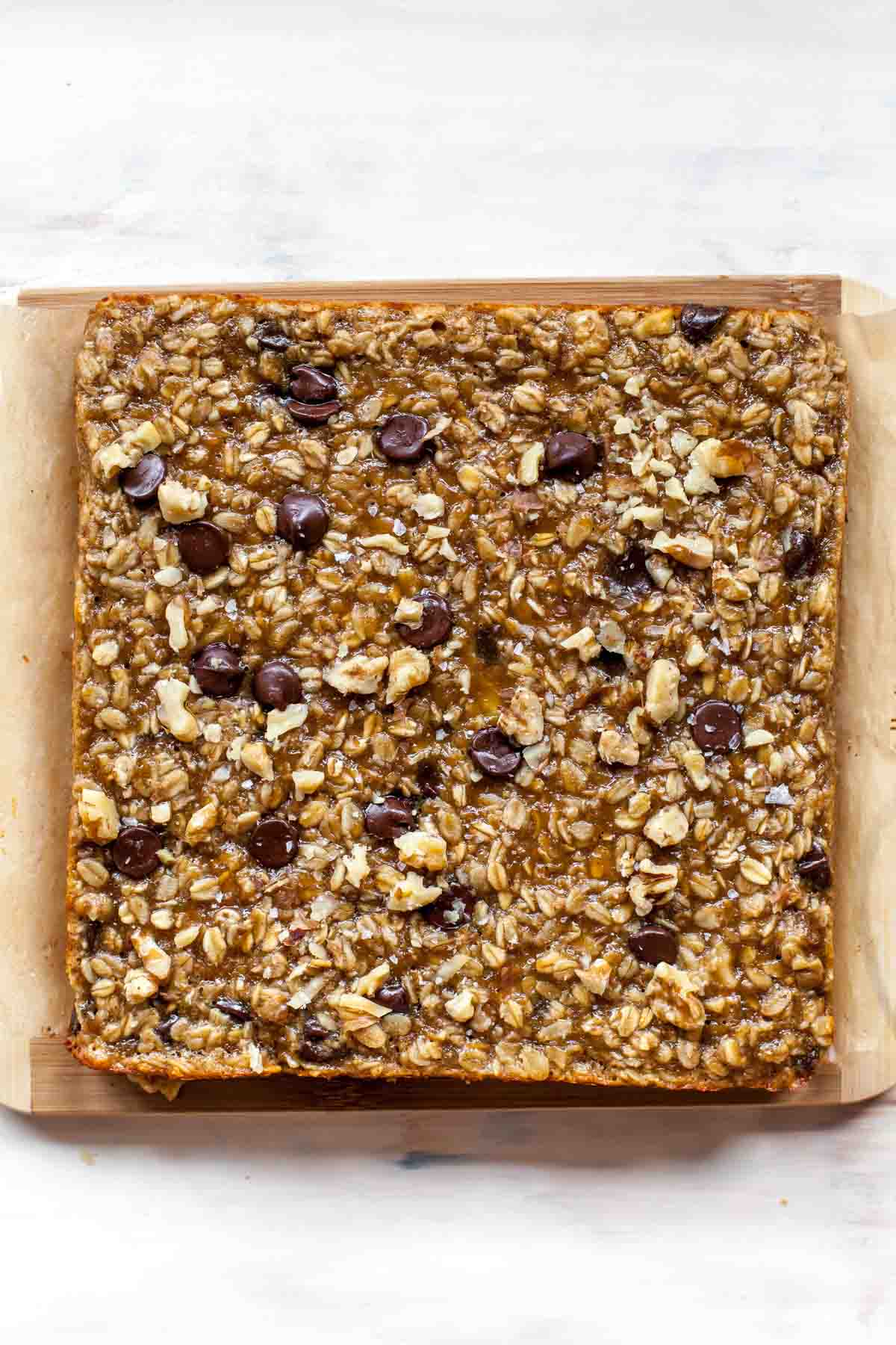Baked banana peanut butter oat bars topped with chocolate chips on a cutting board.