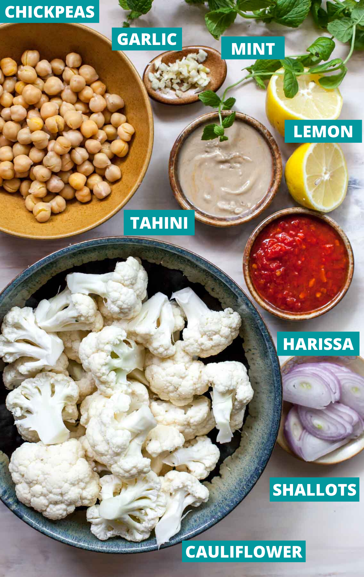 Cauliflower florets, chickpeas, tahini, harissa, and tahini in separate bowls with ingredient label tags