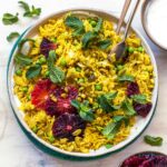 Curry rice in a tan bowl topped with orange slices, fresh mint, and pistachios