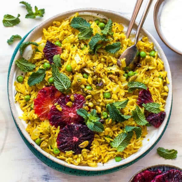 Curry rice in a tan bowl topped with orange slices, fresh mint, and pistachios