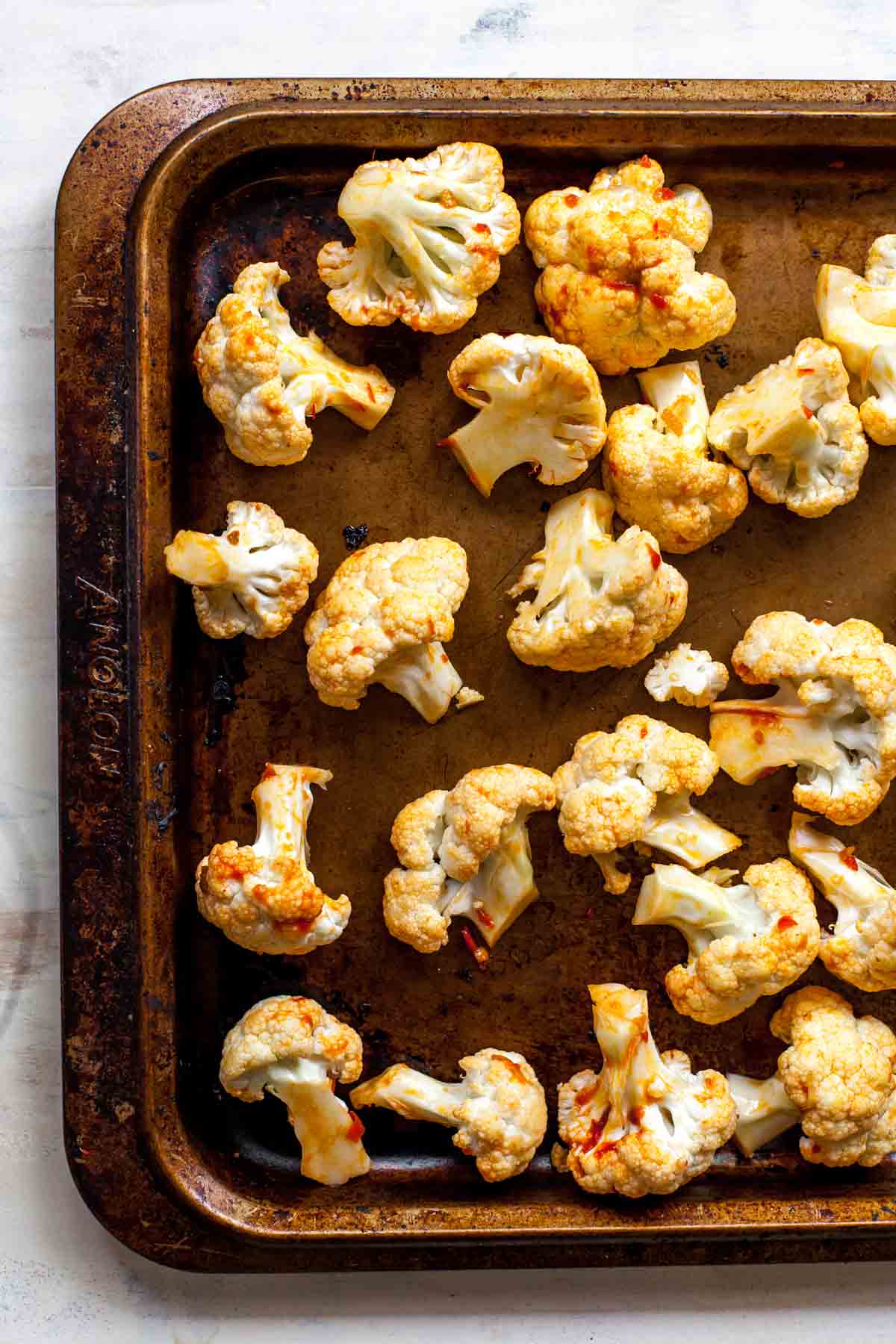 Cauliflower florets on a baking tray tossed in olive oil and red harissa paste