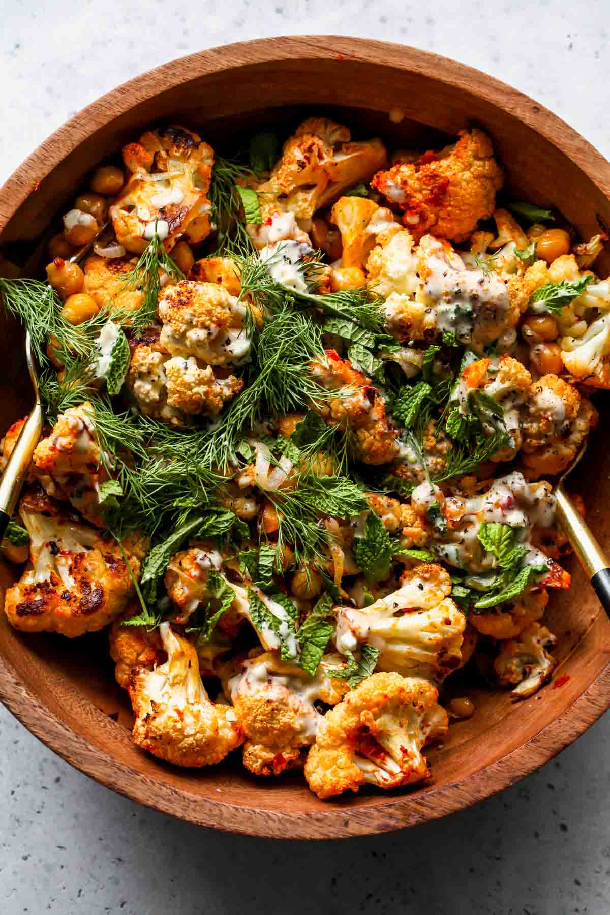 Roasted cauliflower and chickpea salad drizzled with tahini and herbs in a wooden bowl