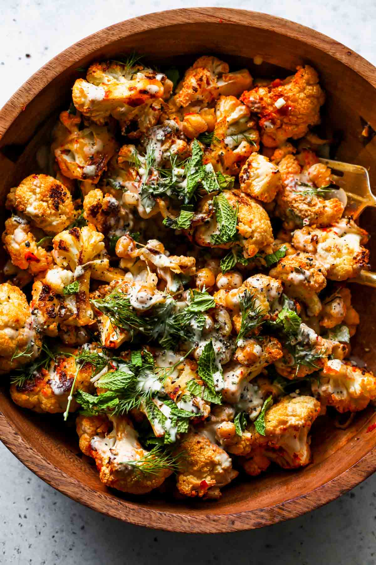 Harissa Roasted Cauliflower and Chickpea Salad with Lemon-Tahini Dressing and herbs in a serving bowl