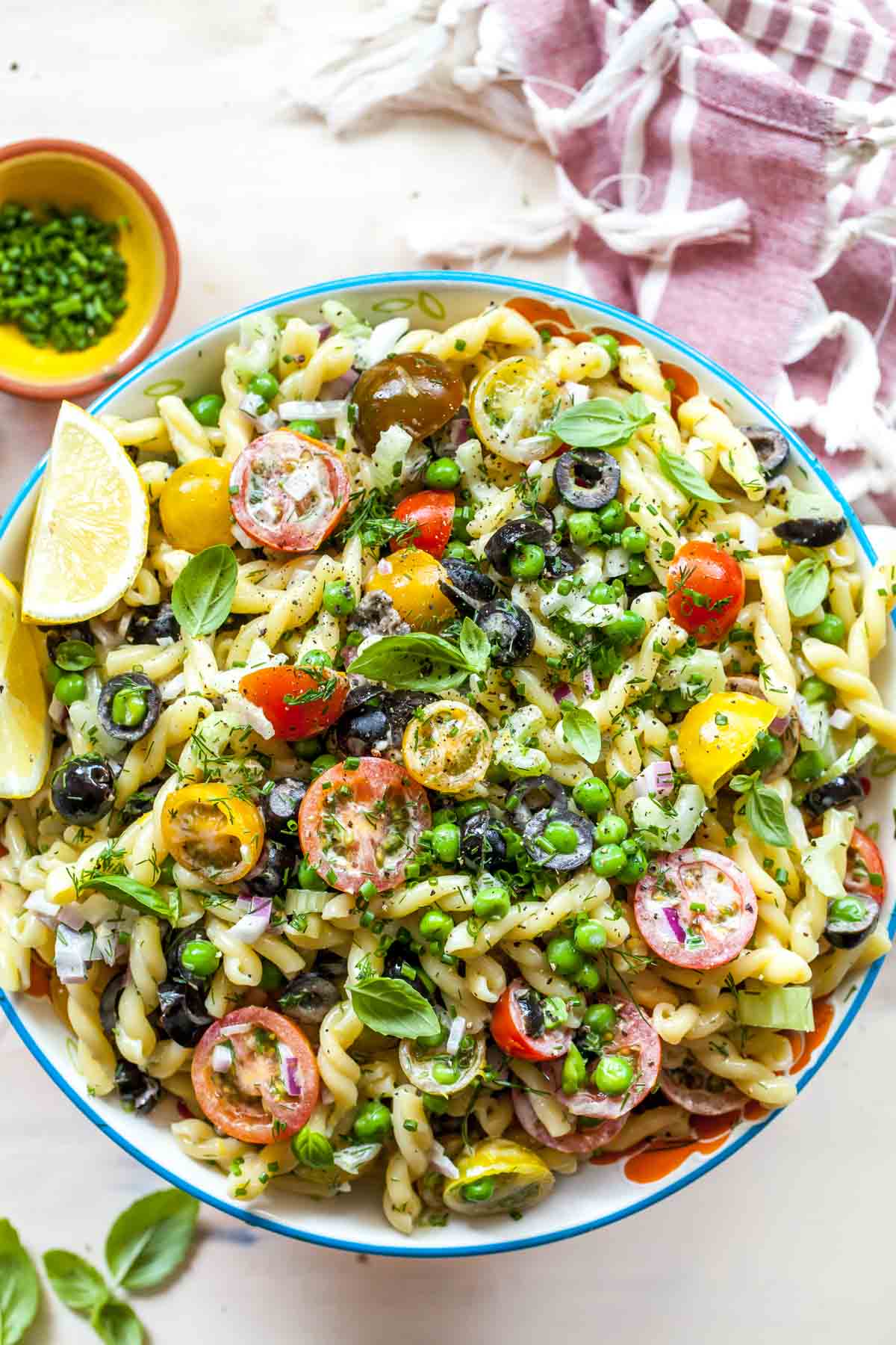 Pasta salad with tomatoes, herbs, and peas in a large bowl with lemon wedge garnish.