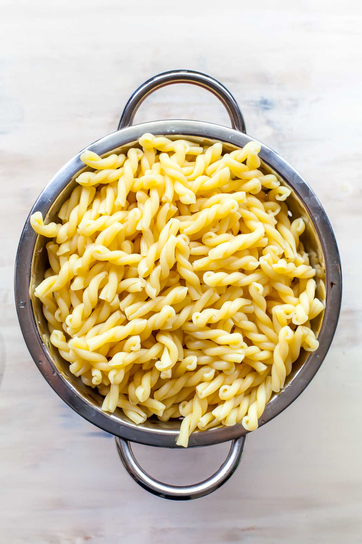 Cooked gemelli pasta in a colander on a tan surface