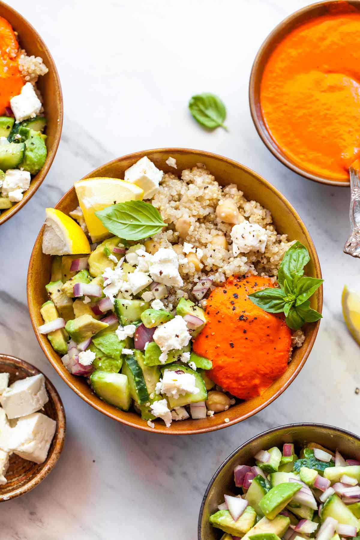 Quinoa, chickpeas, and avocado salad in a gold bowl topped with orange red pepper sauce and basil