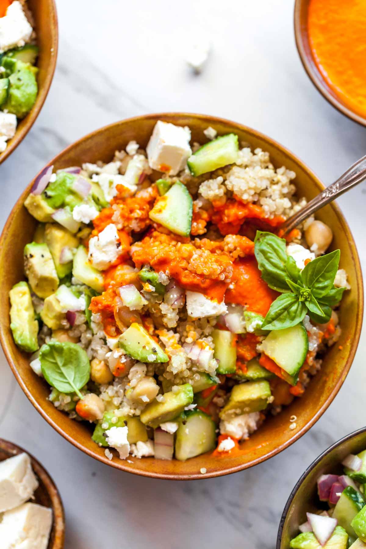 Mediterranean quinoa bowls with red pepper sauce mixed in and spoon resting on the side