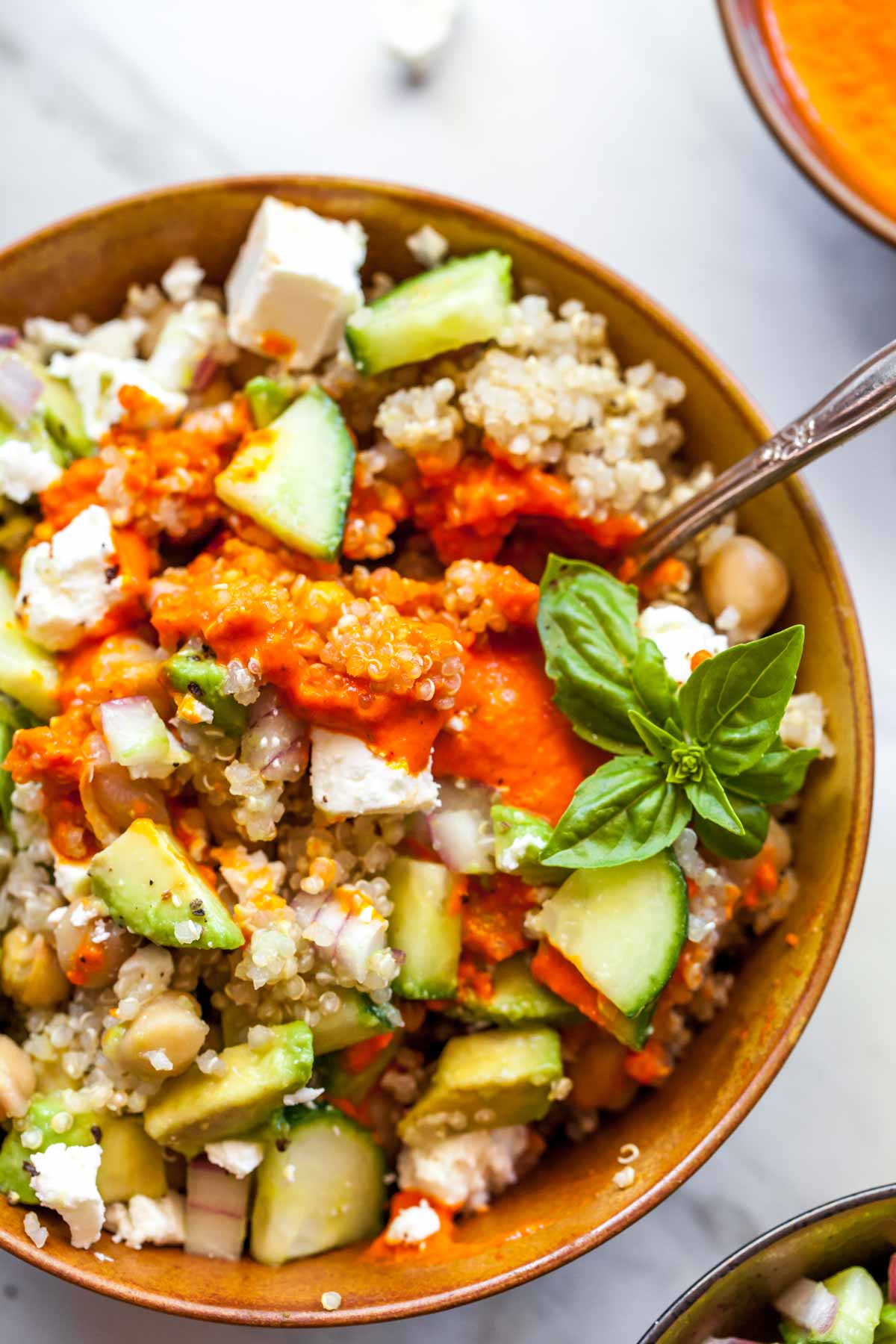 Close up of Mediterranean quinoa bowls with red pepper sauce mixed in and spoon resting on the side