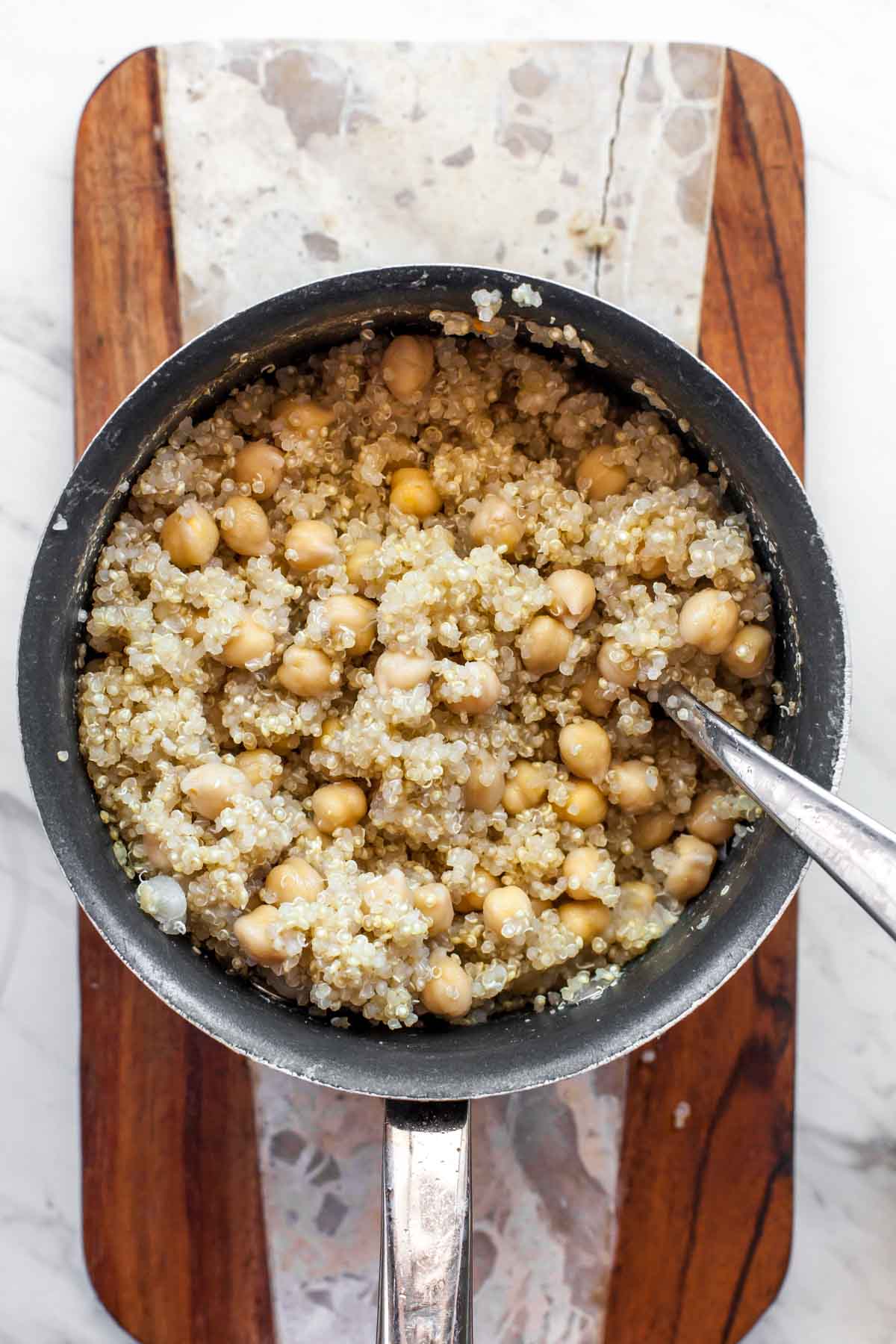 Cooked quinoa and chickpeas in a small pot with spoon resting on the right side